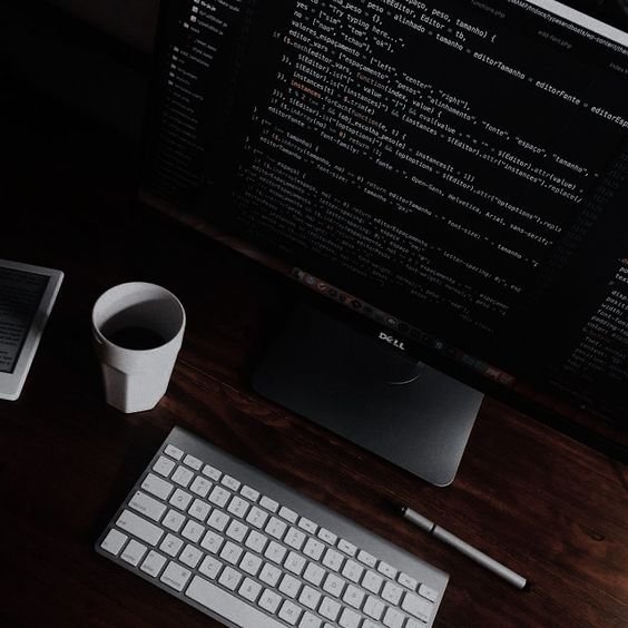  A computer monitor, keyboard, and cup of coffee on a desk.