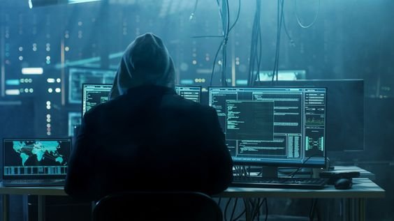 A person in a hoodie sitting at a desk with multiple monitors.