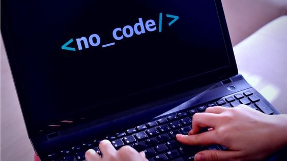 A person typing on a laptop with a black screen displaying the text "", symbolizing the no-code movement in app development.