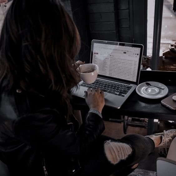 A woman sitting at a table, working on a laptop and sipping coffee, engaged in flutter development.