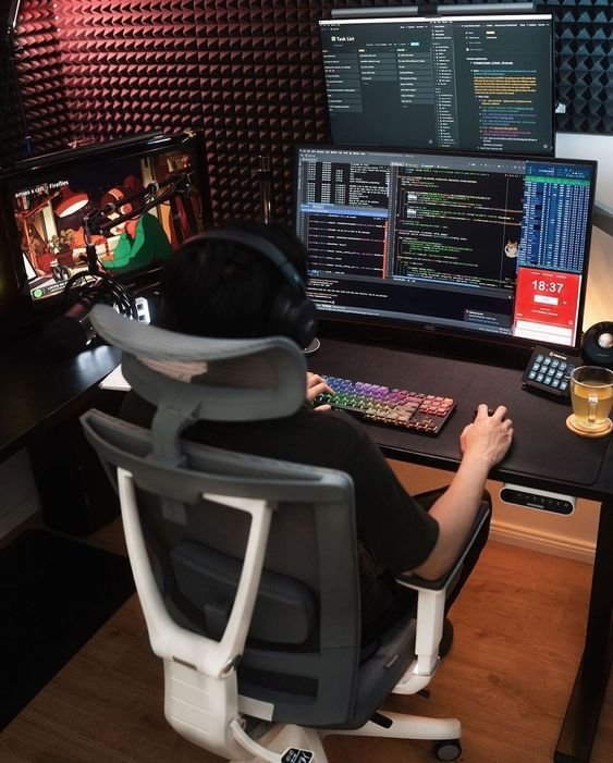 A man sitting at a desk with two monitors and a computer, working on flutter development.