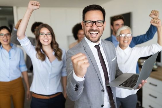 A diverse group of professionals in business attire smiling and raising glasses in celebration.